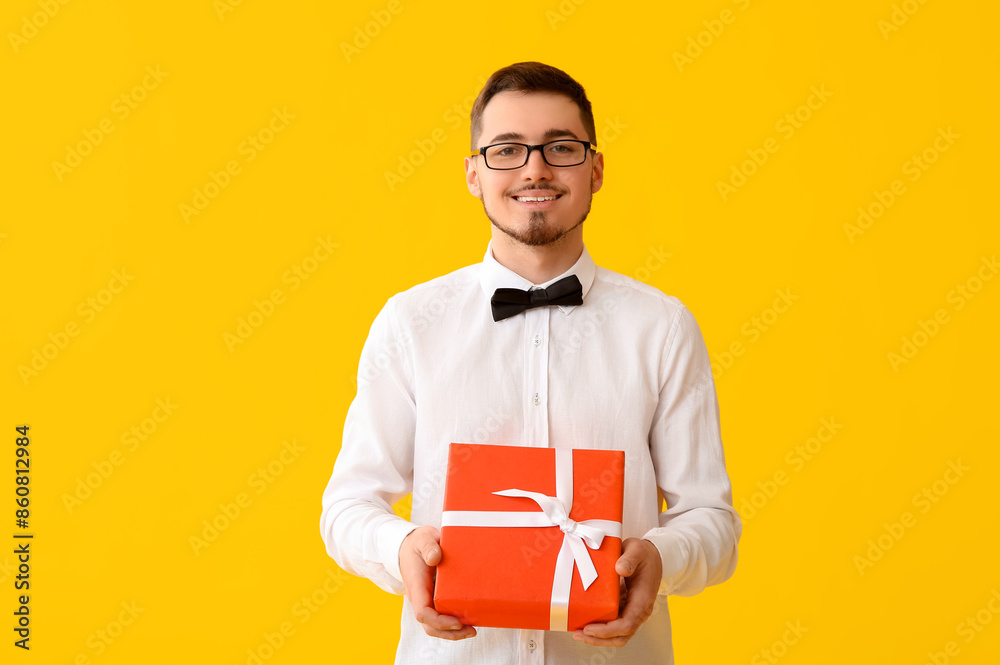 Handsome man with gift box on yellow background Handsome man with gift box on yellow background