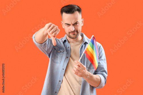 Angry young man with LGBT flag showing thumb-down on orange background. Accusation concept