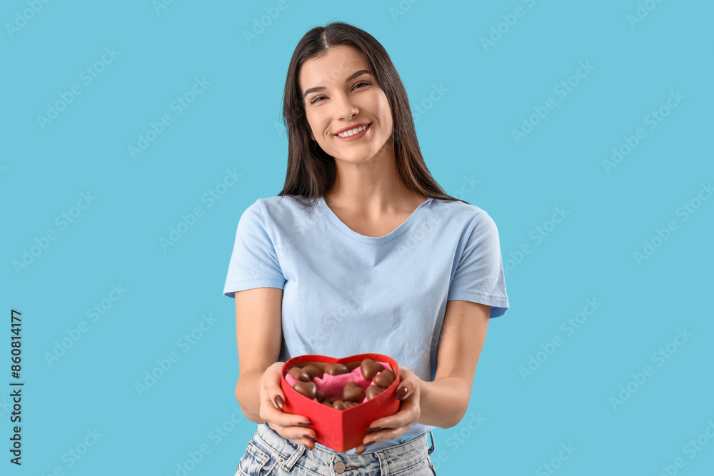 Young woman with box of heart-shaped chocolate candies on blue background Young woman with box of heart-shaped chocolate candies on blue background