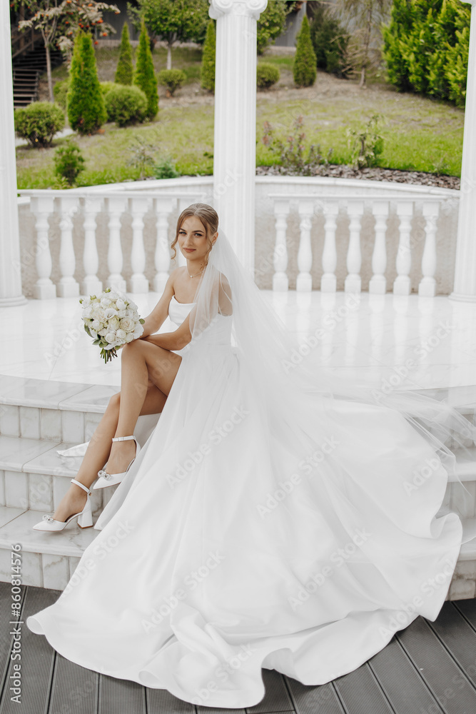 A bride is sitting on a set of steps wearing a white dress and holding a bouquet. Concept of elegance and romance, as the bride is dressed in a wedding gown and is surrounded by flowers. The setting A bride is sitting on a set of steps wearing a white dress and holding a bouquet. Concept of elegance and romance, as the bride is dressed in a wedding gown and is surrounded by flowers. The setting
