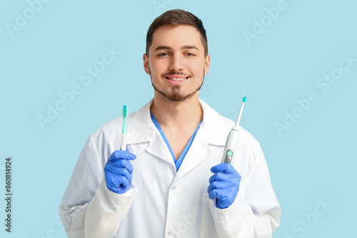 Male dentist with different toothbrushes on turquoise background