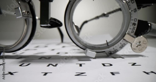 Optometric glasses for measuring visual acuity lie on paper Snellen chart. Medical equipment for checking eyesight waits for patient in doctor office