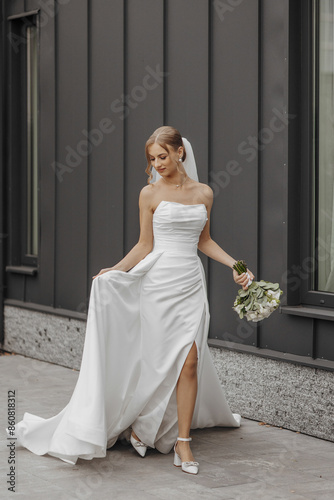A woman in a white wedding dress is walking down a street holding a bouquet of flowers. Concept of elegance and celebration, as the bride is dressed in her wedding attire
