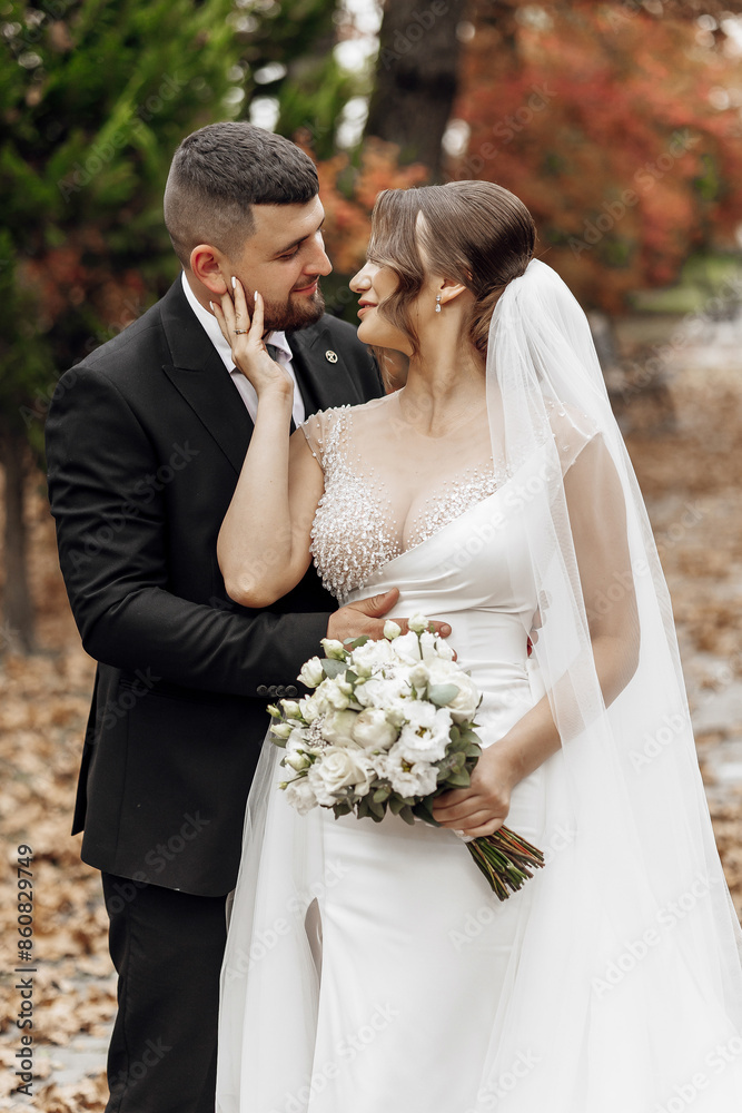 A bride and groom are standing together, embracing each other. The bride is wearing a white dress and the groom is wearing a black suit. The scene is set in a garden A bride and groom are standing together, embracing each other. The bride is wearing a white dress and the groom is wearing a black suit. The scene is set in a garden