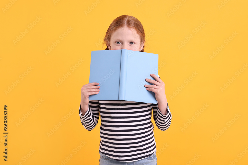 Cute little girl with book on yellow background