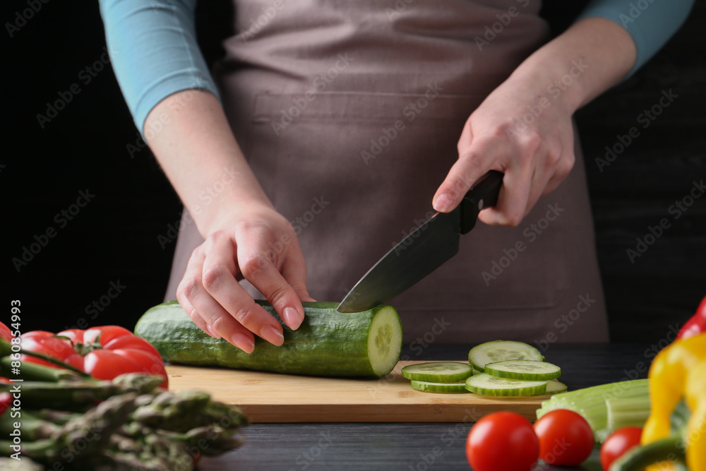 Healthy food. Woman cutting cucumber at black wooden table, closeup Healthy food. Woman cutting cucumber at black wooden table, closeup