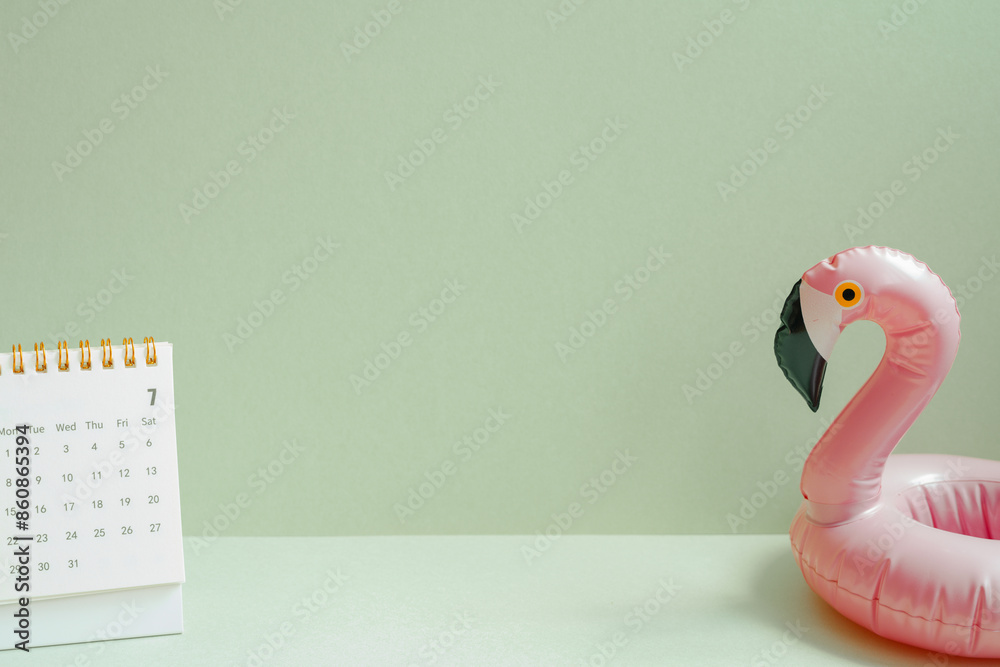 Summer vacation planning concept. Pink flamingo bird shape swimming pool tube and calendar on mint green background