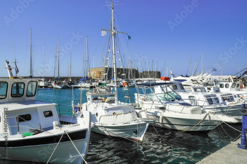 Sailing boats in front of ancient fortress under deep blue sky in the famous ancient sea port of Agios Nikolaos, Crete Island, Greece