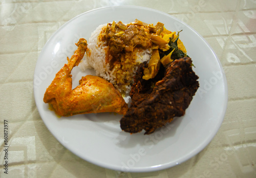 A plate of Padang Rice, served with chicken curry, fried lungs, and vegetables, a very famous specialty from West Sumatra Province, Indonesia. photo