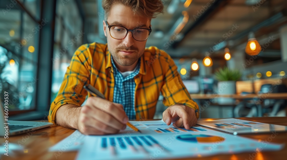Focused man analyzing business charts. Focused man with glasses in a yellow plaid shirt analyzes business charts and data in a modern office setting. Focused man analyzing business charts. Focused man with glasses in a yellow plaid shirt analyzes business charts and data in a modern office setting.