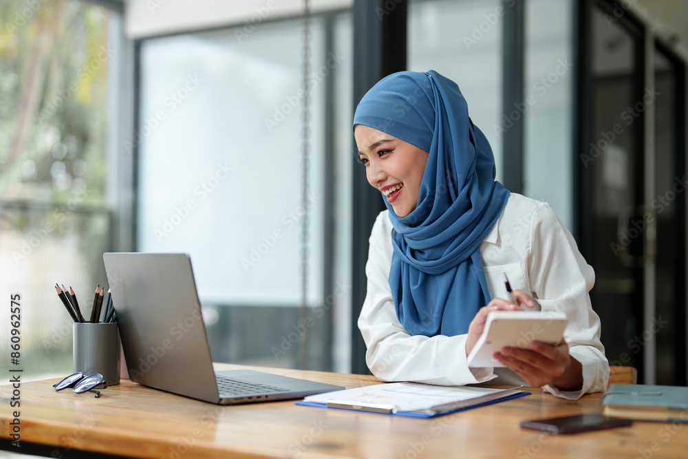 Modern office Muslim businesswoman wearing hijab sits with laptop online, doing paperwork Sitting and working on financial projects, analysis, calculations, startup business ideas, e-commerce, online. Modern office Muslim businesswoman wearing hijab sits with laptop online, doing paperwork Sitting and working on financial projects, analysis, calculations, startup business ideas, e-commerce, online.