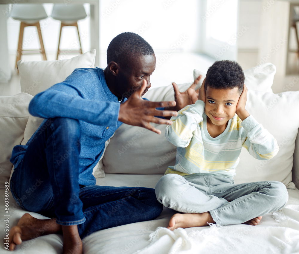 Black Boy Covering Ears While Angry Father Shouting At Him Standing At Home. Domestic Violence And Unhappy Childhood. Black Boy Covering Ears While Angry Father Shouting At Him Standing At Home. Domestic Violence And Unhappy Childhood.