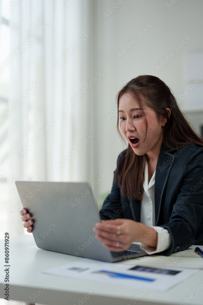 Surprised and happy businesswoman shows joyful expression after viewing news results, business approval results and financial approval results on laptop at office. Startup business growth concept. Surprised and happy businesswoman shows joyful expression after viewing news results, business approval results and financial approval results on laptop at office. Startup business growth concept.