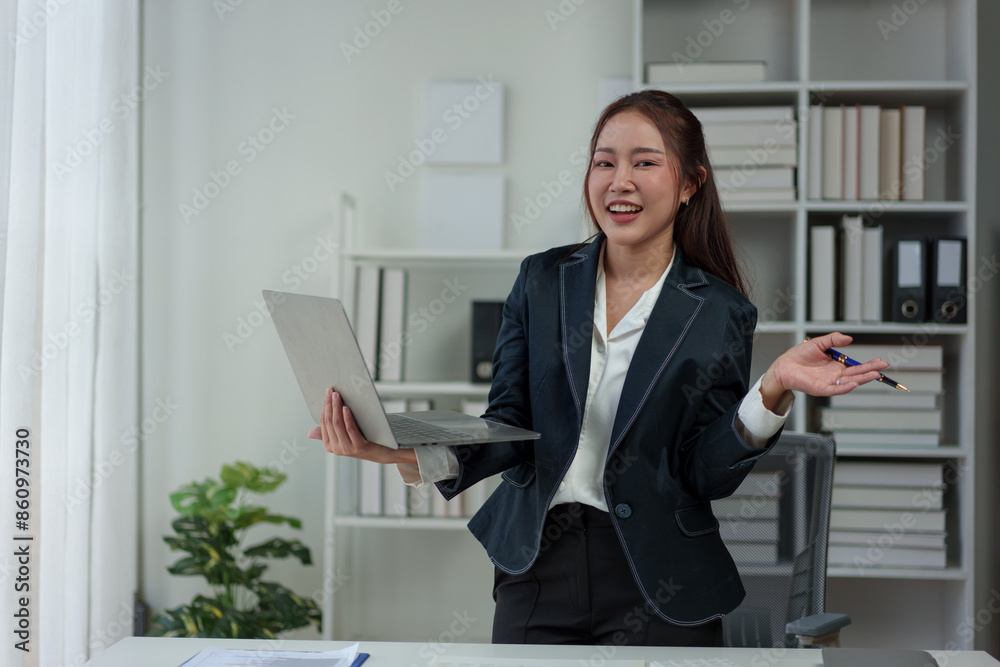 Cheerful and confident Asian businesswoman stands presenting bar chart data from a laptop folder in an online meeting in the office. Startup business ideas, accounting, online marketing. Cheerful and confident Asian businesswoman stands presenting bar chart data from a laptop folder in an online meeting in the office. Startup business ideas, accounting, online marketing.