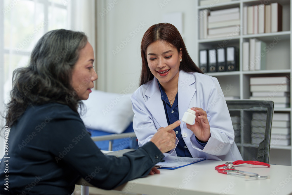 Fototapeta premium Doctor, female pharmacist points to a medicine bottle, gives advice, recommends how to take medicine to an elderly female patient. Explaining prescriptions, medical system concepts and health care.