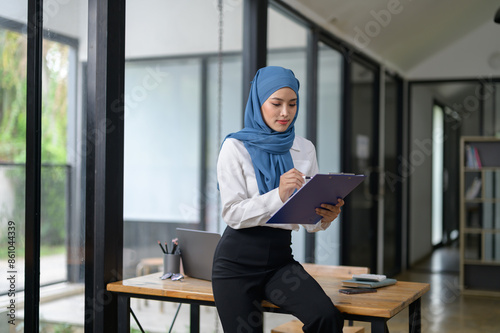 Asian Muslim businesswoman using a file to write notes Work record Woman working at tax office, accounting, online marketing startup business idea.