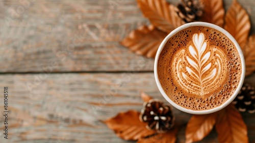 Top view of a latte with intricate foam art, surrounded by autumn leaves and pinecones on a rustic wooden table. Cozy fall coffee vibe.