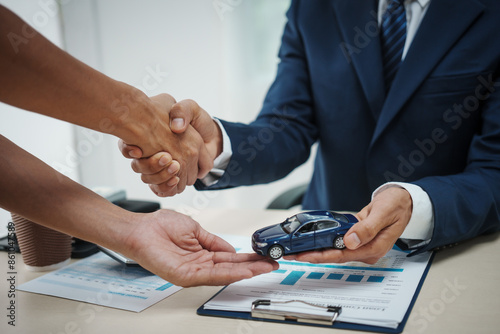 A man in a suit works at his desk selling cars and online car insurance with low interest rates, offering car loans, vehicle financing, comprehensive coverage, and shaking hands with clients.