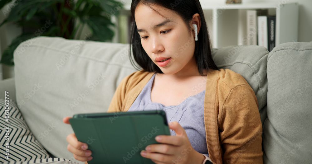 Portrait of Relaxed young Asian woman wear wireless headphones listen to music and playing digital tablet on the sofa in the living room at morning ,Free time Portrait of Relaxed young Asian woman wear wireless headphones listen to music and playing digital tablet on the sofa in the living room at morning ,Free time