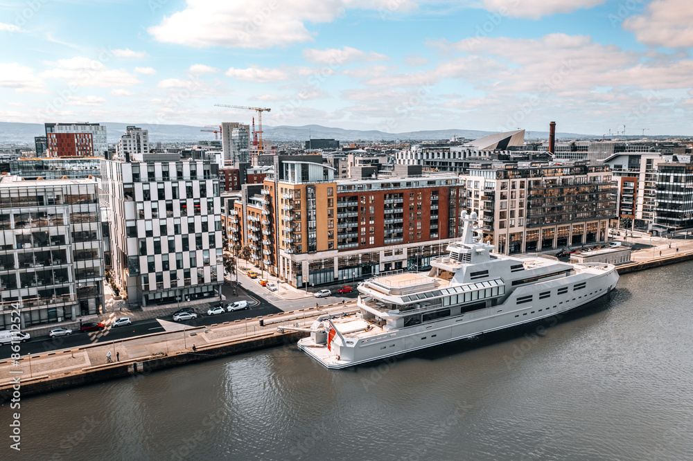 Naklejka premium Modern Waterfront in Dublin Featuring Luxury Yacht, Contemporary Architecture, and Scenic Urban Landscape under Clear Blue Sky