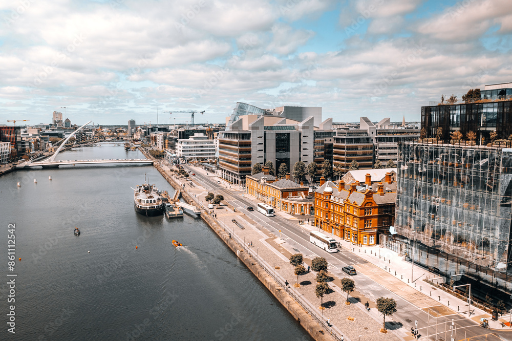 Fototapeta premium Modern Waterfront Cityscape in Dublin with Scenic River View, Contemporary Architecture, and Vibrant Urban Life under Clear Summer Sky.