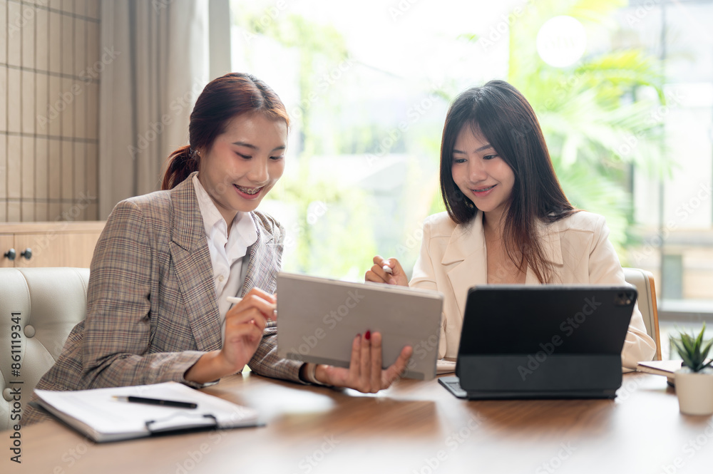 Two Asian businesswomen are discussing work on their digital tablets, having an informal meeting. Two Asian businesswomen are discussing work on their digital tablets, having an informal meeting.