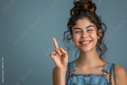 Cheerful Young Woman Pointing Upward in Casual Denim Outfit Against Blue Background photo