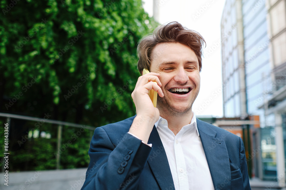Cheerful businessman talking on smart phone in front of trees and building Cheerful businessman talking on smart phone in front of trees and building