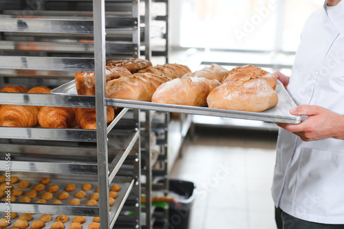 Male baker holding a tray of baked breads in bakery shop photo