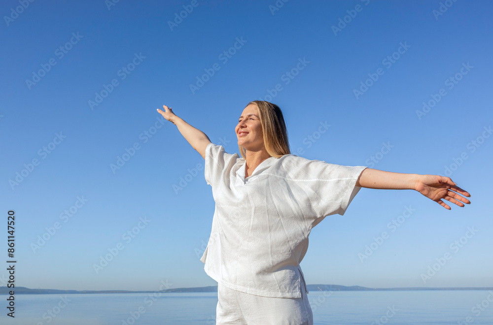 Smiling woman standing with arms outstretched under blue sky at beach Smiling woman standing with arms outstretched under blue sky at beach