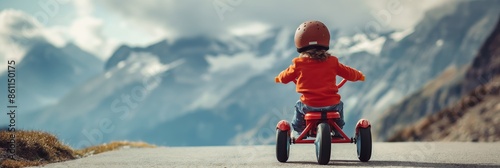 A child in an orange jacket and helmet riding a red tricycle on a road with majestic mountains in the background on a partly cloudy day.