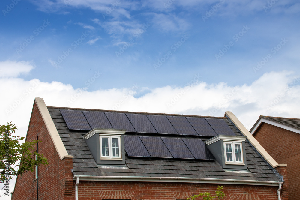 Photo of a modern British house in the UK with electrical solar panels on the roof on a bright sunny day with clouds in the sky