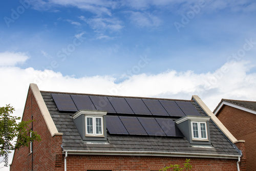 Obraz na płótnie Photo of a modern British house in the UK with electrical solar panels on the roof on a bright sunny day with clouds in the sky w salonie