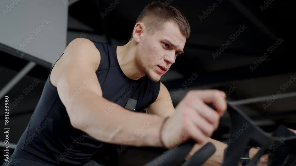 A serious young male athlete intensely works out on a rowing machine in a modern gym, displaying determination and strength. Focused Young Man Using a Rowing Machine at the Gym A serious young male athlete intensely works out on a rowing machine in a modern gym, displaying determination and strength. Focused Young Man Using a Rowing Machine at the Gym
