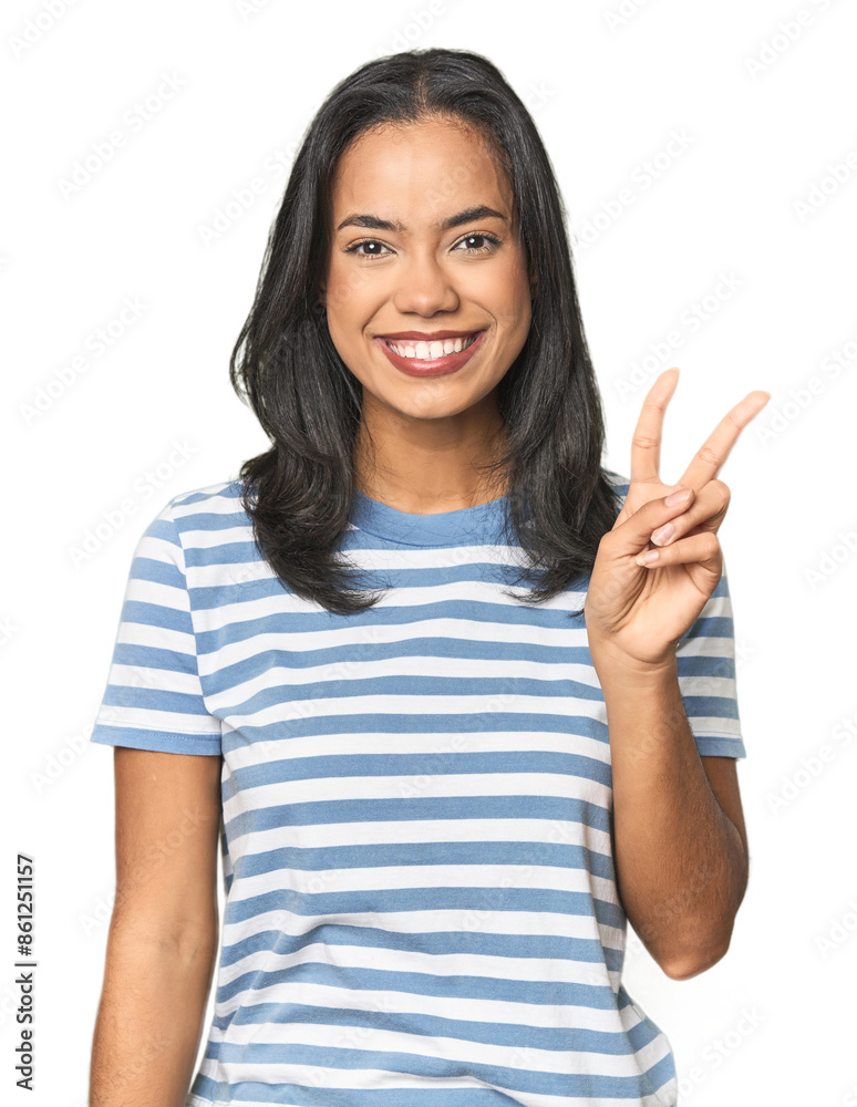 Young Latina posing in studio showing victory sign and smiling broadly. Young Latina posing in studio showing victory sign and smiling broadly.
