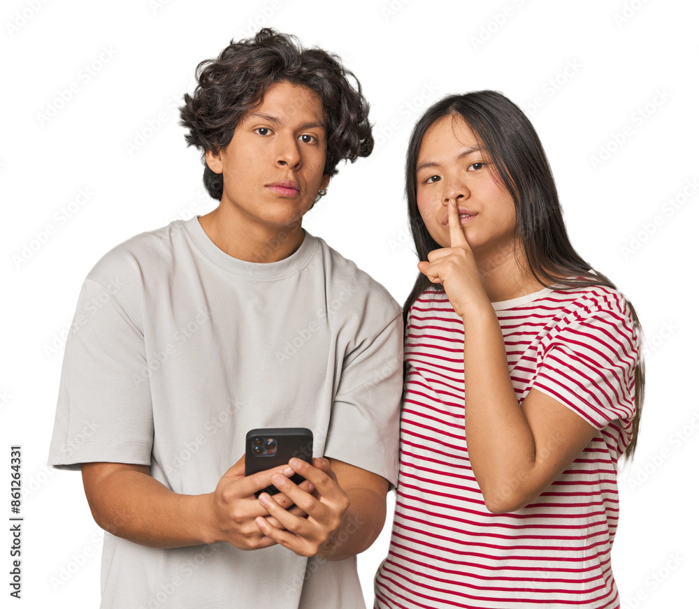 Young interracial couple using smartphone keeping a secret or asking for silence. Young interracial couple using smartphone keeping a secret or asking for silence.