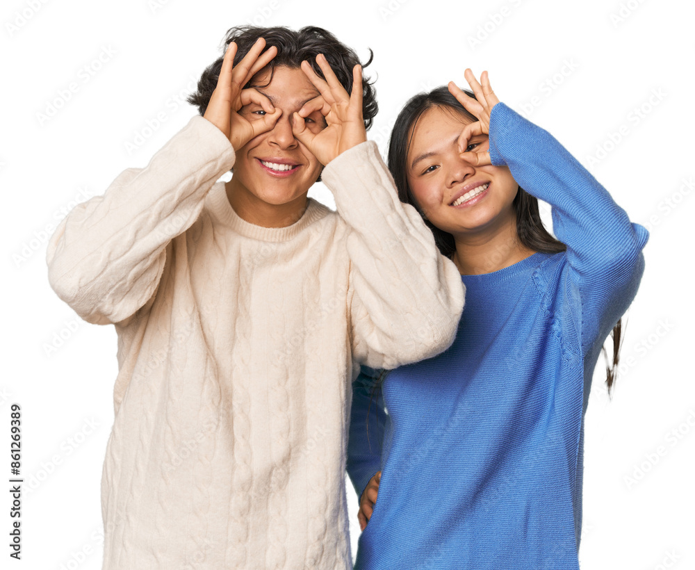 Young interracial couple in studio showing okay sign over eyes Young interracial couple in studio showing okay sign over eyes