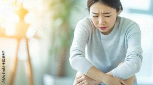 Free Download Unhappy Asian Woman Suffering from Knee Pain in Bright Living Room with Soft Natural Light Streaming Through Windows - GFXLoad