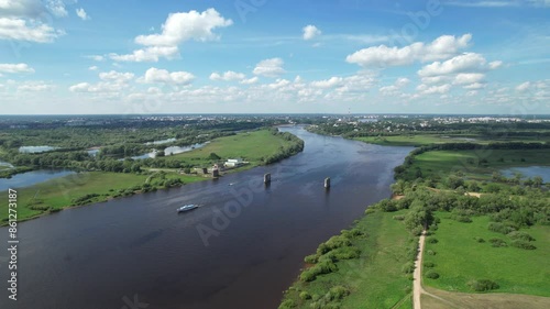 Flying a drone over the Volkhov River with a view of the destroyed bridge and the city of Veliky Novgorod in the distance on a sunny summer day. River boat trips