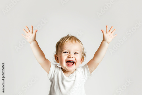 Beautiful baby boy in a white T-shirt raised his hands up and sitting on white background. Close up. Copy space. Baby emotions.