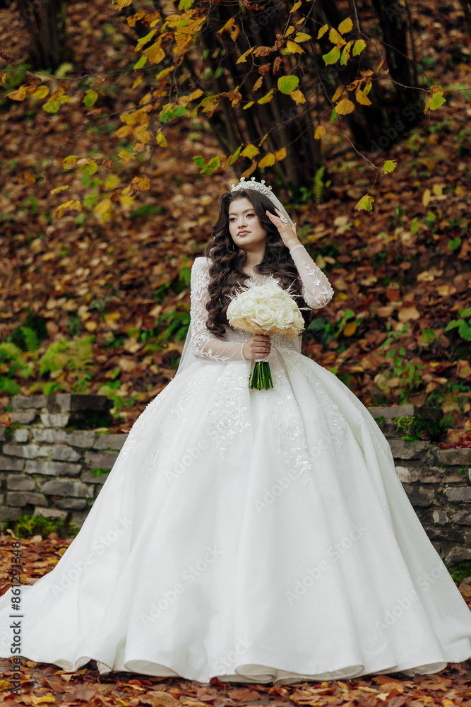 A woman in a white dress is holding a bouquet of flowers. She is standing in a forest with leaves on the ground A woman in a white dress is holding a bouquet of flowers. She is standing in a forest with leaves on the ground