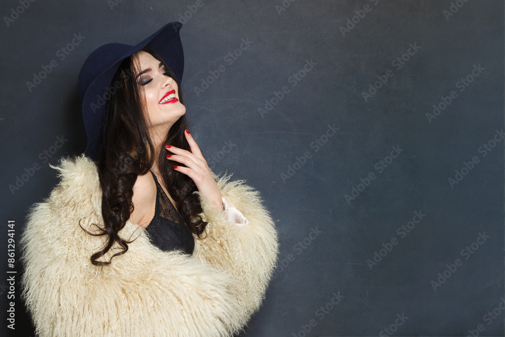 Joyful young adult woman fashion model with bright make-up and long wavy hair wearing blue hat posing against blue studio wall background Joyful young adult woman fashion model with bright make-up and long wavy hair wearing blue hat posing against blue studio wall background