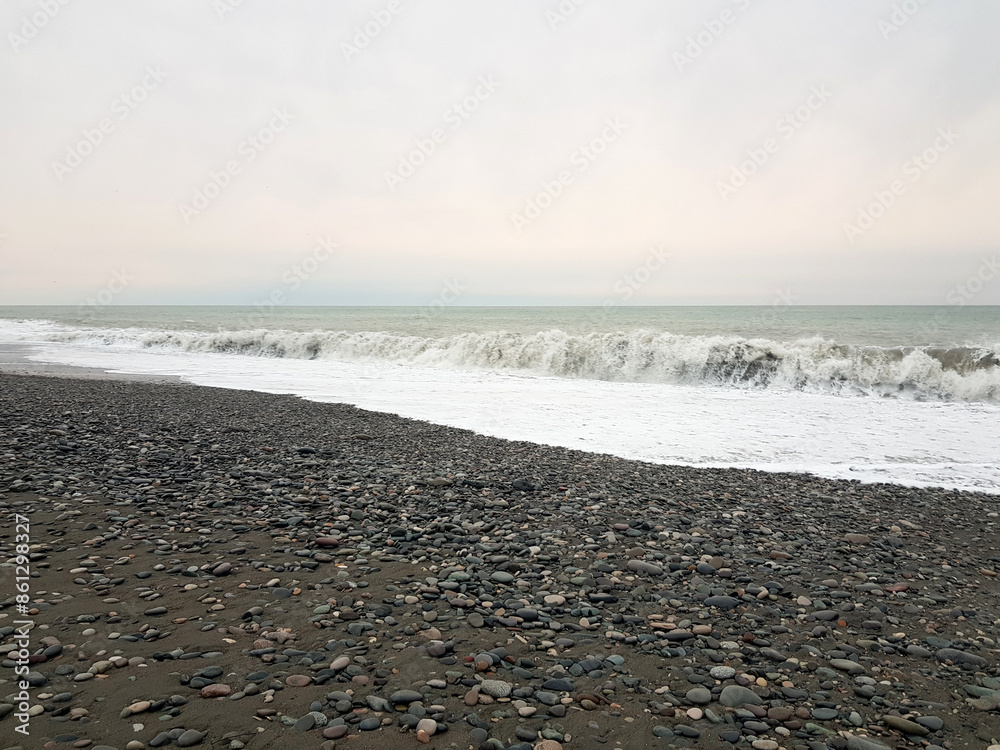 Dramatic cold ocean background with sea wave and beach with black sand and stones Dramatic cold ocean background with sea wave and beach with black sand and stones