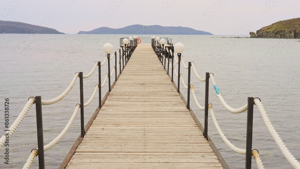 Naklejka premium A wooden pier stands by water, offering peaceful view of serene lake. The calm water reflects sky, creating a tranquil atmosphere. Ideal for themes involving water, relaxation, and nature's beauty.