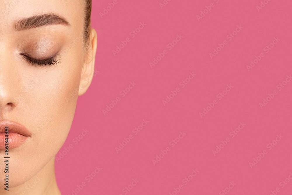 Obraz premium Woman half-face with her eyes closed. The woman face is only partially visible, showing her closed eyes, brow, nose, and lips. The background is a solid, bright pink color, copy space