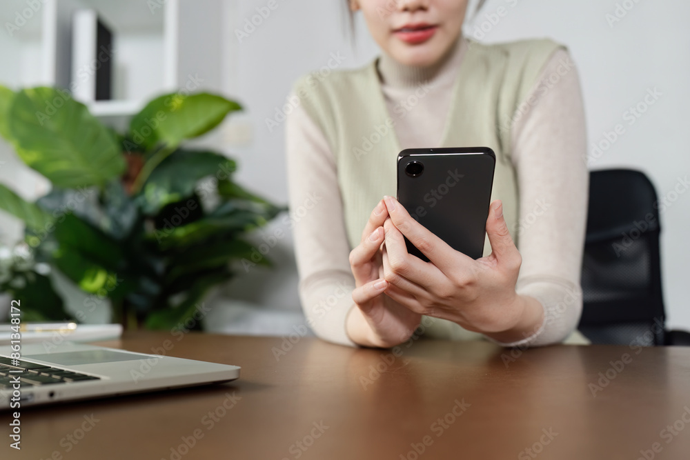 Young Professional Woman Working Remotely from Home Office Using Smartphone and Laptop, Green Plant in Background