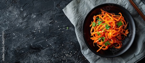 Square black ceramic dish showing Korean carrot salad strips with vegetables, round straw napkins, and copy space image; Korean dish popular in Russian cuisine. photo