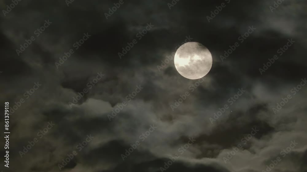 Full Moon in a dramatic night sky with dark clouds. Natural gloomy night skyscape in moonlight. Real video recording through a telephoto lens Full Moon in a dramatic night sky with dark clouds. Natural gloomy night skyscape in moonlight. Real video recording through a telephoto lens