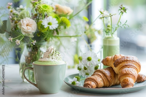 A beautifully arranged breakfast scene with a matcha latte, croissants, and a vase of fresh flowers. 