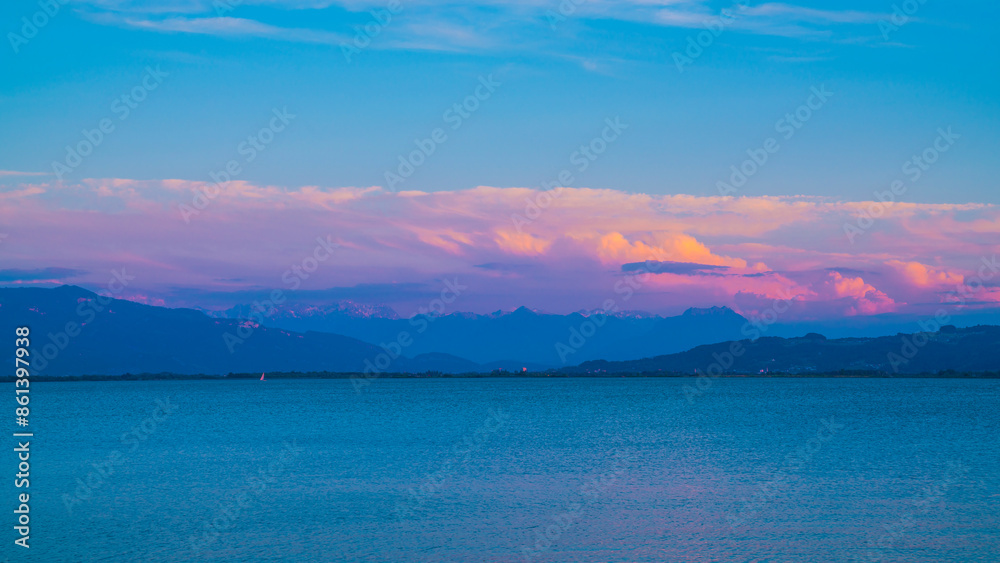 Germany, Warm sunset light on alps mountains nature landscape behind silent water of bodensee lake after sunset, panorama view from lindau